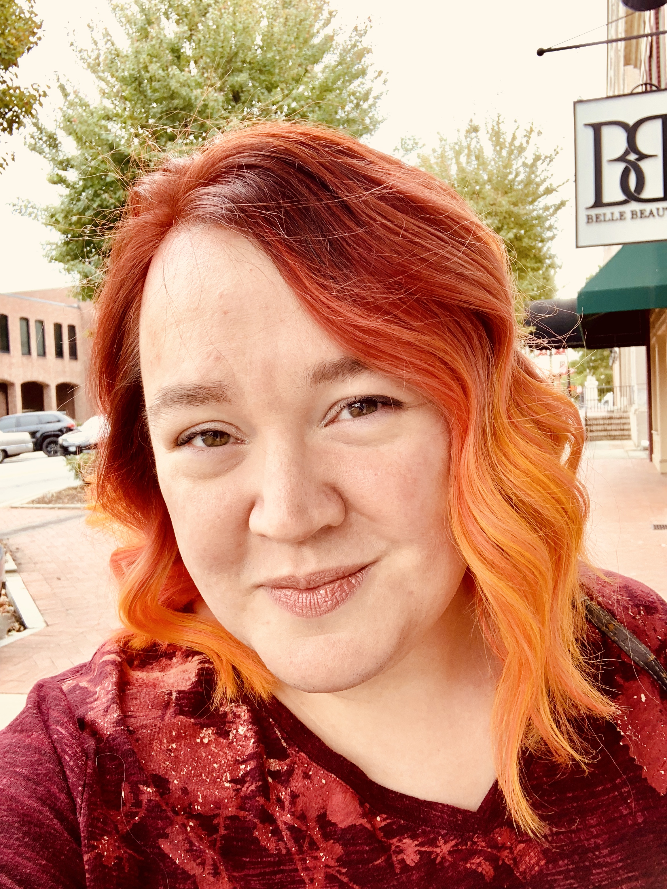 photo of me; my hair is tones of orange; I'm a white woman standing downtown in my hometown on a pretty fall day